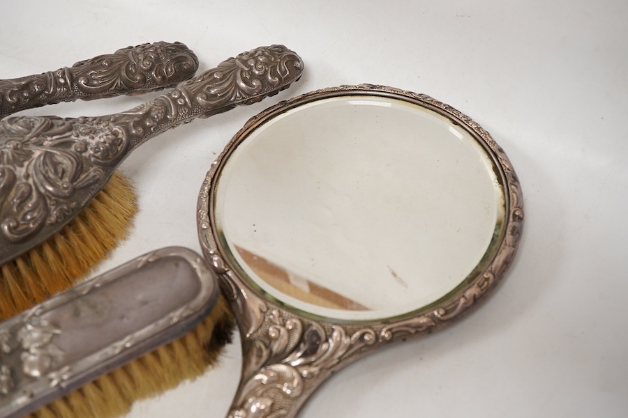 Four assorted early 20th century repousse silver mounted dressing table items to include a hand mirror, two hair brushes and a clothes brush(a.f.).